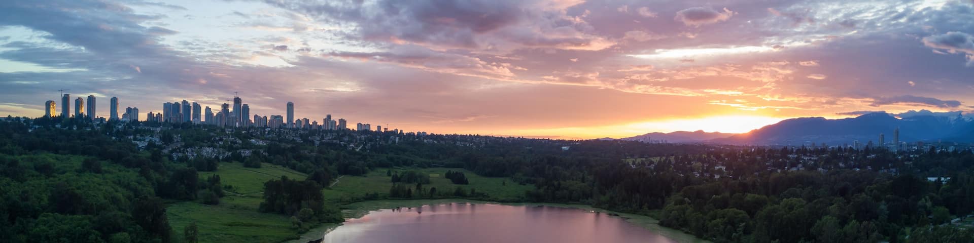 A city skyline at sunset with a lake reflecting the sky.
