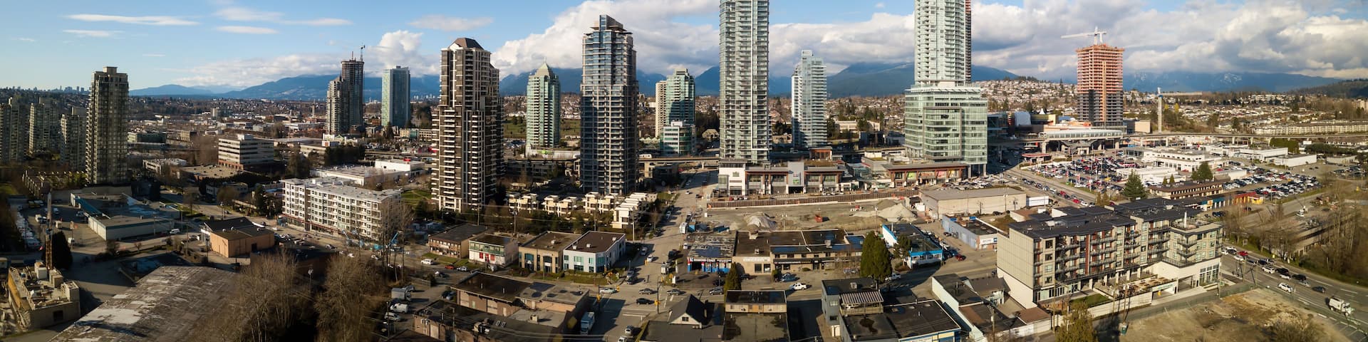 A cityscape with multiple high-rise buildings, a construction crane, and a mountainous backdrop.