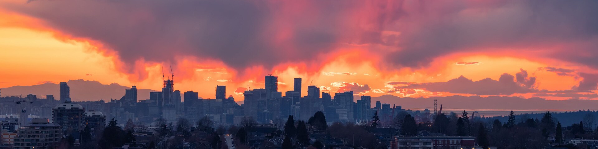 Silhueta urbana ao pôr do sol, com nuvens dramáticas.