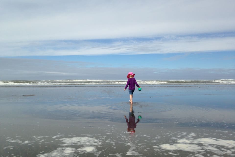 A child walking on a wet beach with waves in the background.