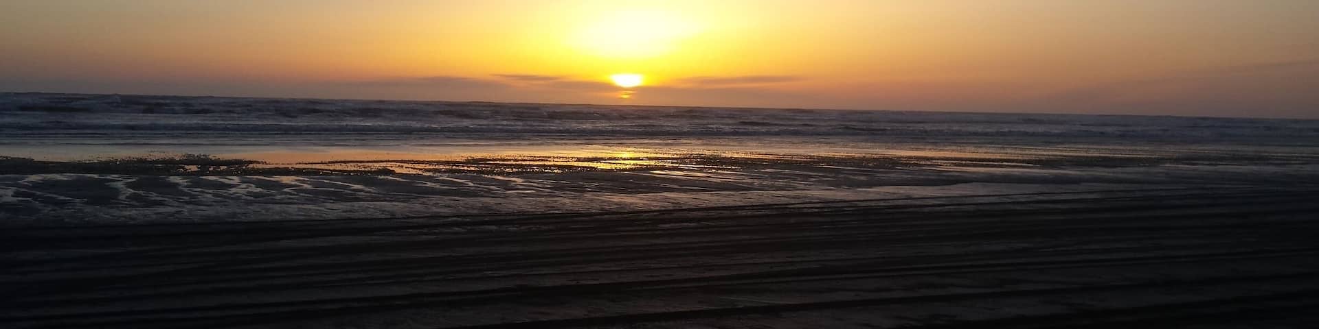 A sunset over a beach with waves and a clear sky.