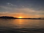 Een zonsondergang boven een kalm meer, met bergen op de achtergrond.