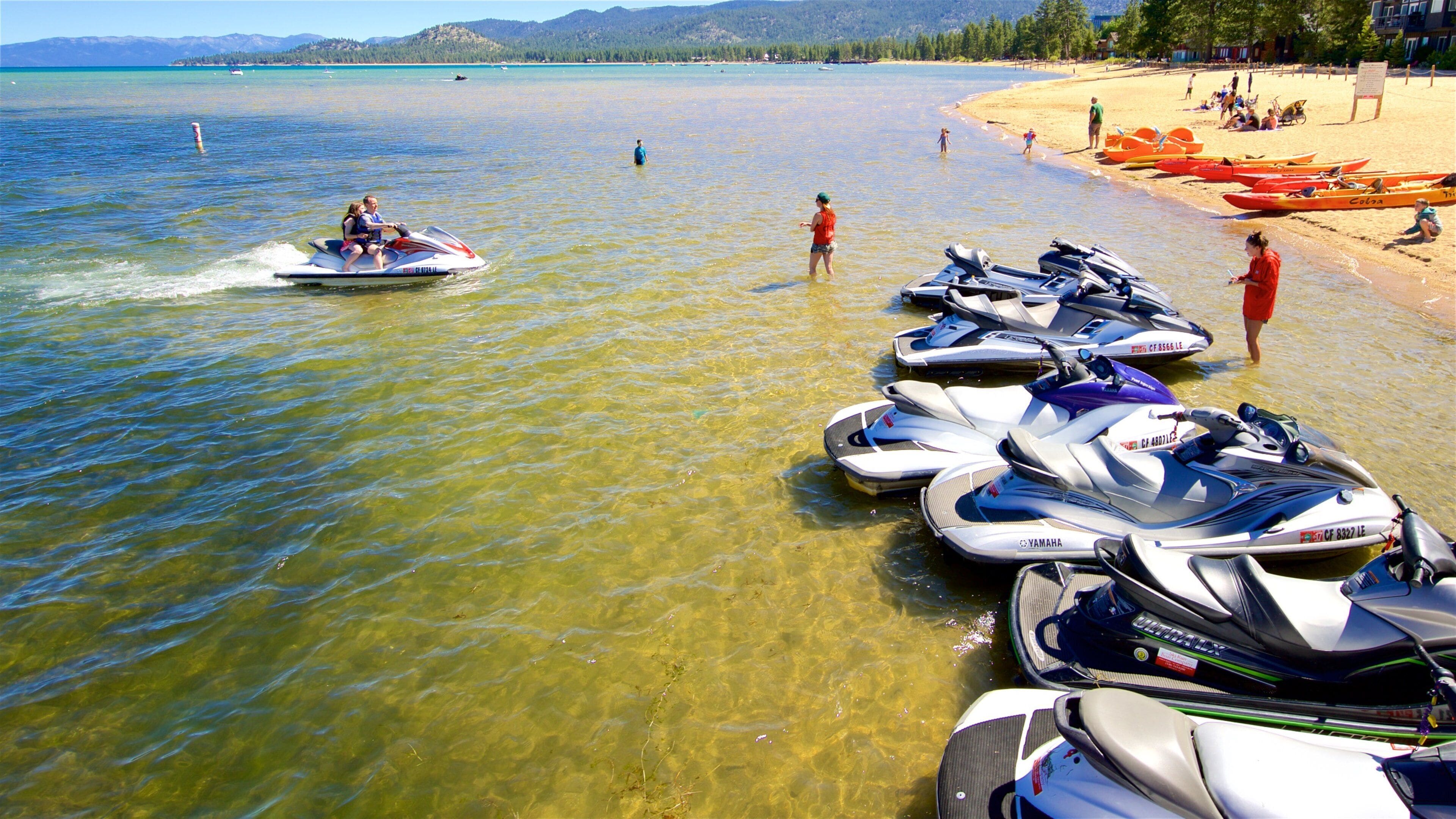 A lake with clear water, a jet ski in motion, and several watercraft docked on the shore.