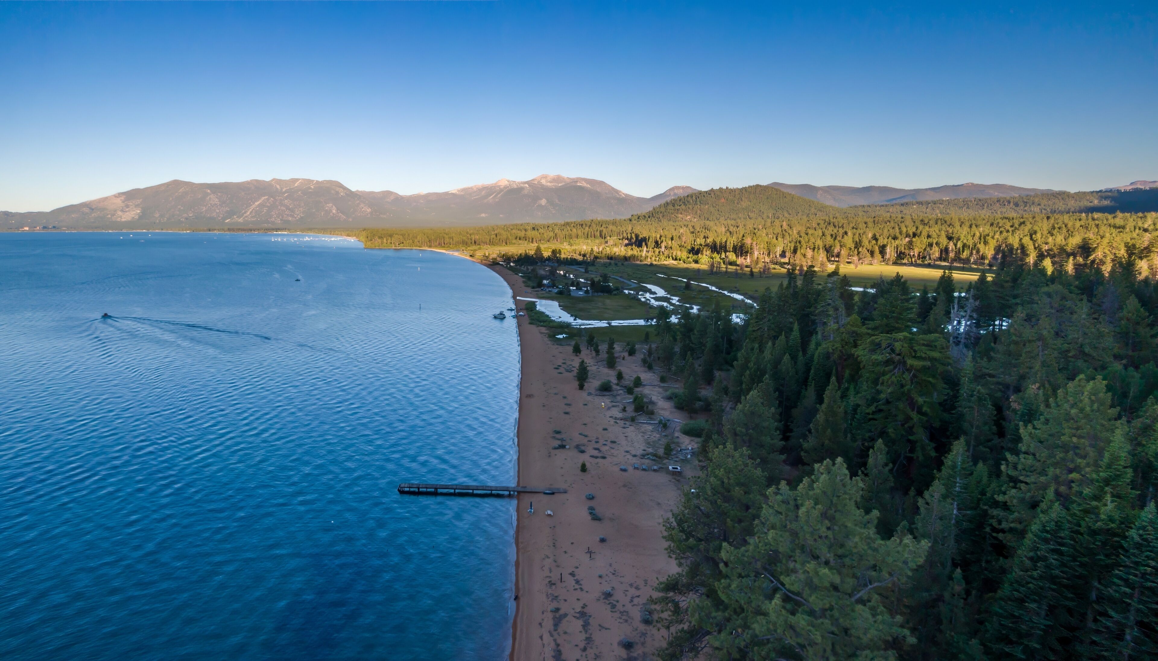 A coastal landscape with a beach, forested area, and mountains in the background.