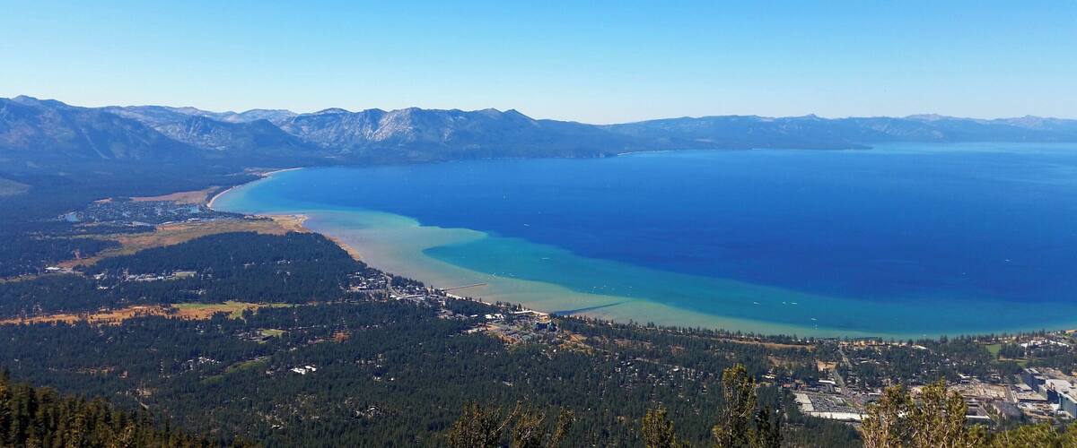 A coastal landscape with a large body of water, a forested area, and a mountain range in the background.