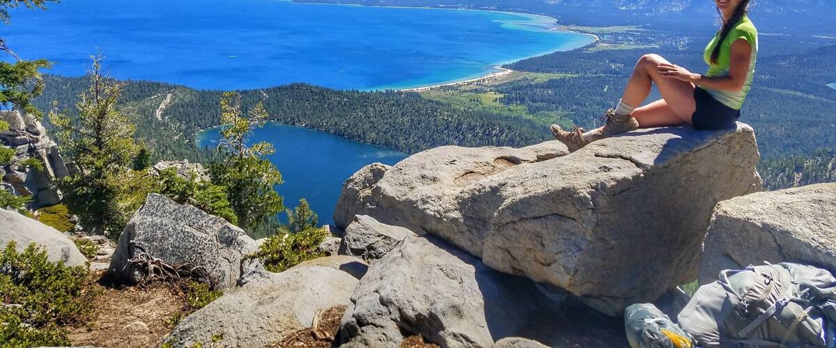 A woman sitting on a rock overlooking a lake surrounded by mountains.