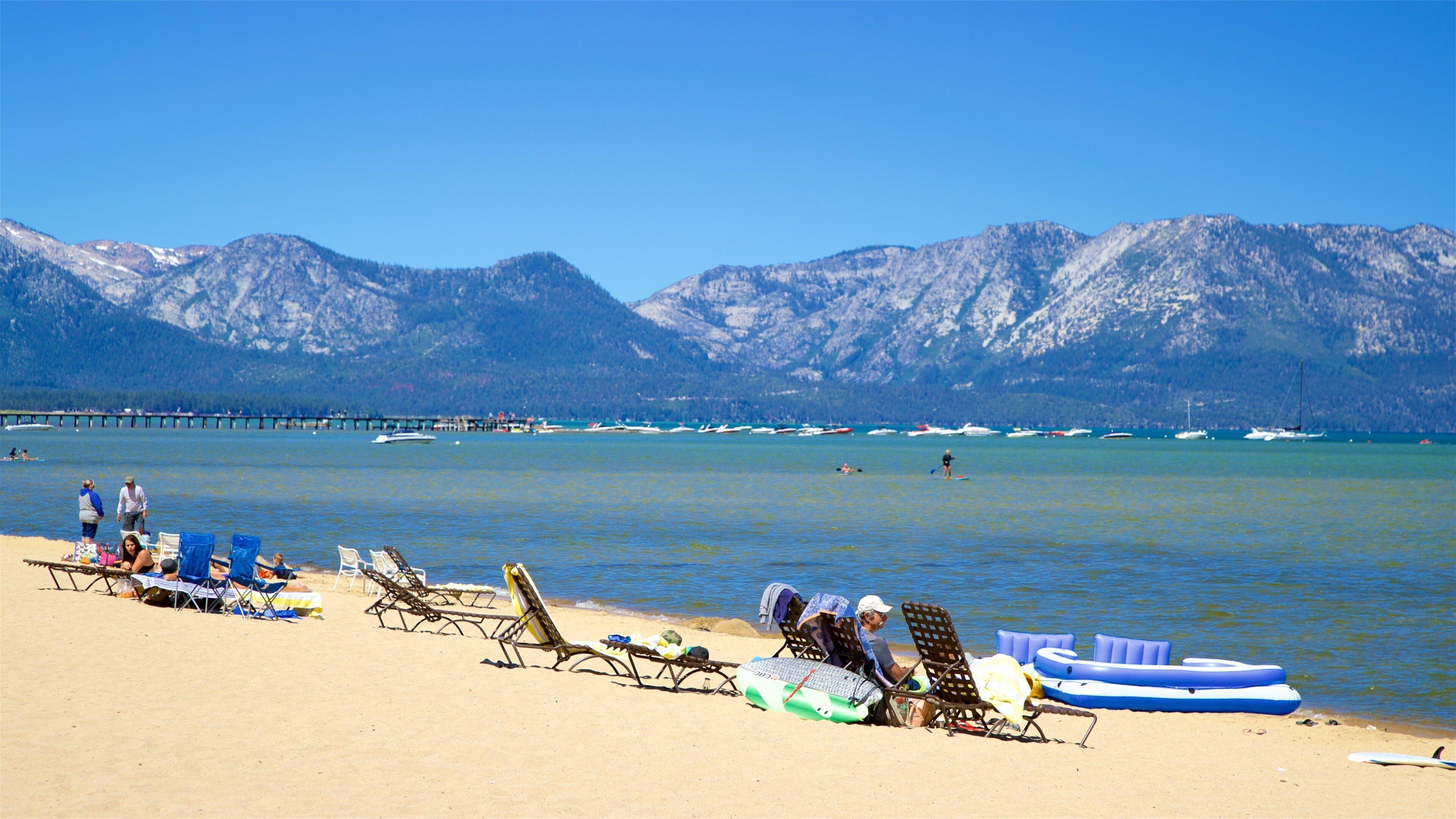 Une plage avec une eau d’un bleu limpide, des montagnes en arrière-plan et plusieurs bateaux.