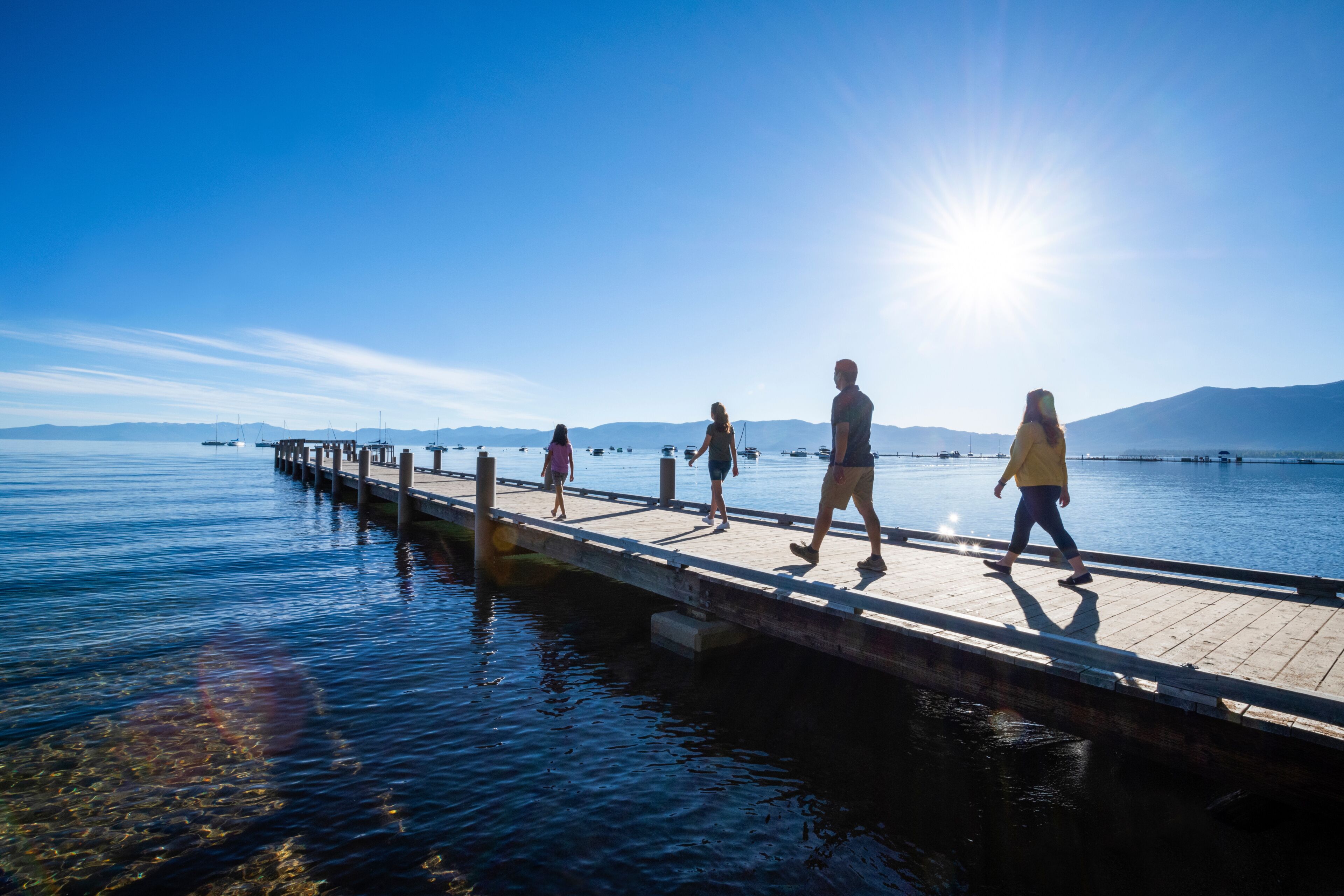 Un muelle de madera que se adentra en aguas tranquilas, con gente caminando a lo largo de él, bajo un cielo despejado.