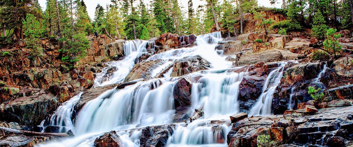 A multi-tiered waterfall surrounded by dense forest.
