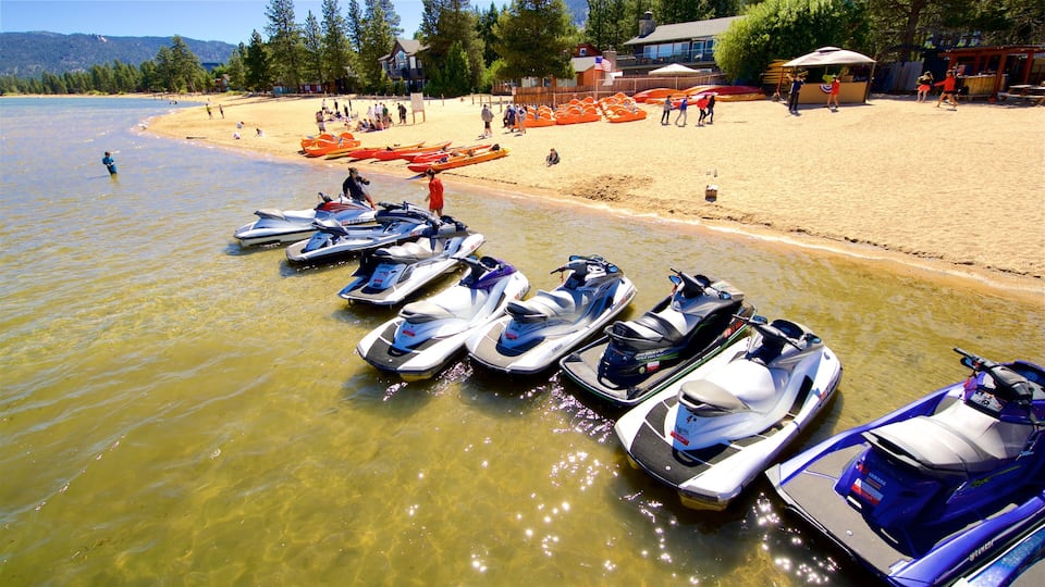 A lakeside with jet skis lined up on the shore, a sandy beach, and a row of orange canoes.