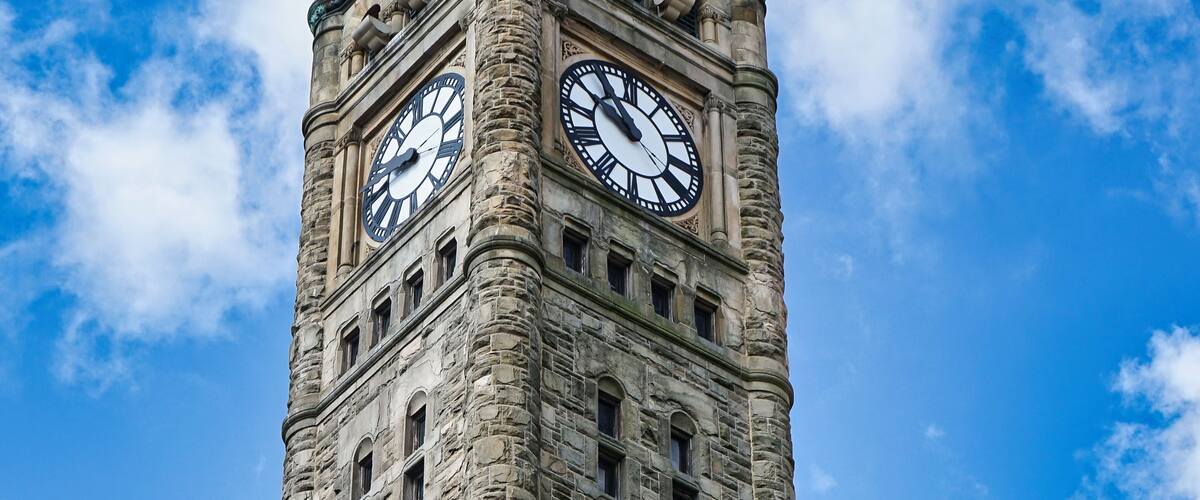 A tall stone clock tower with two clocks, set against a blue sky with clouds.