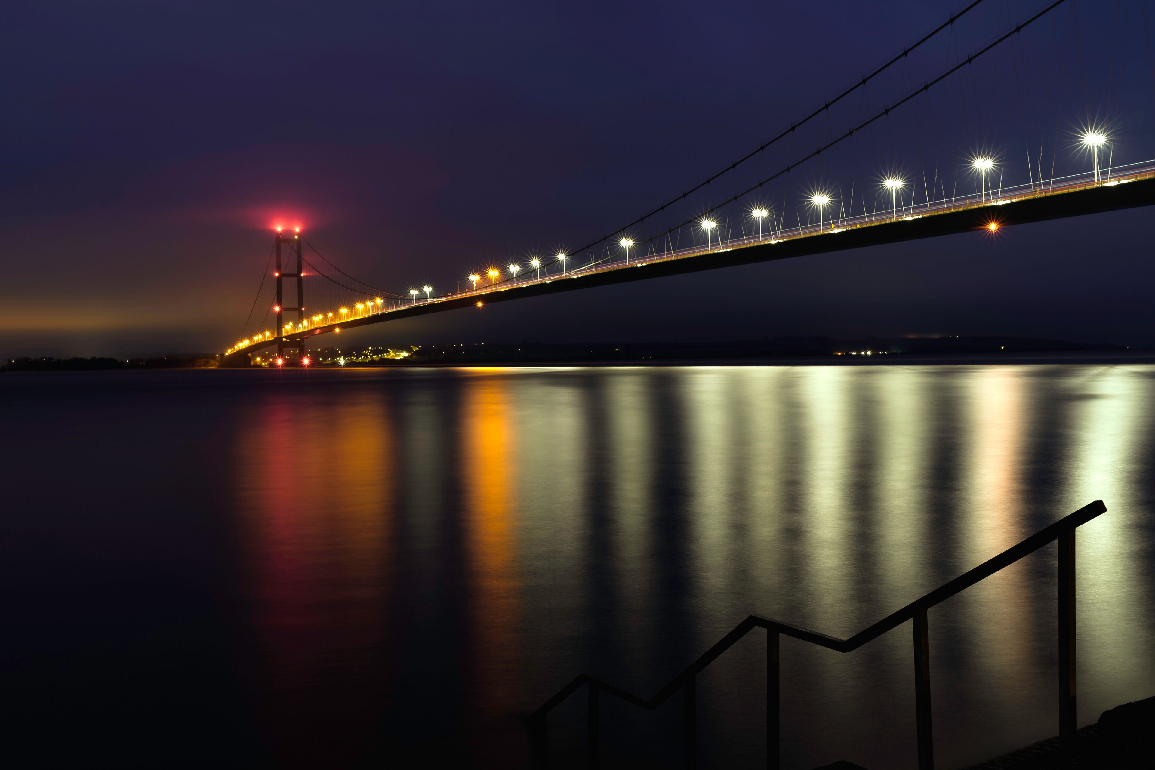 Une vue nocturne d’un pont dont les lumières se reflètent sur l’eau.