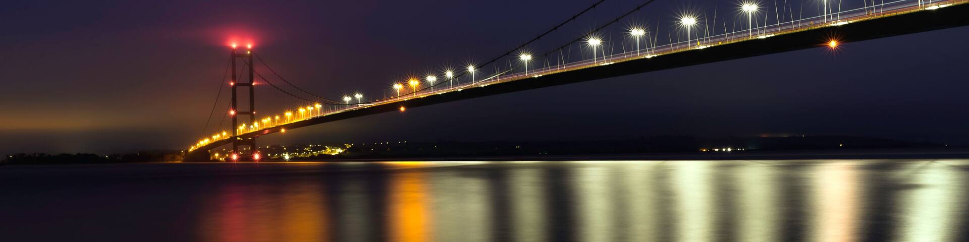 A nighttime view of a bridge with lights reflecting on the water.