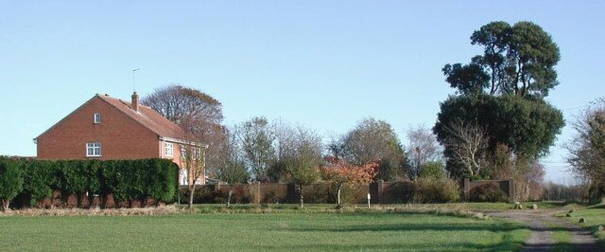 A grassy field with a path, a red house, and trees.