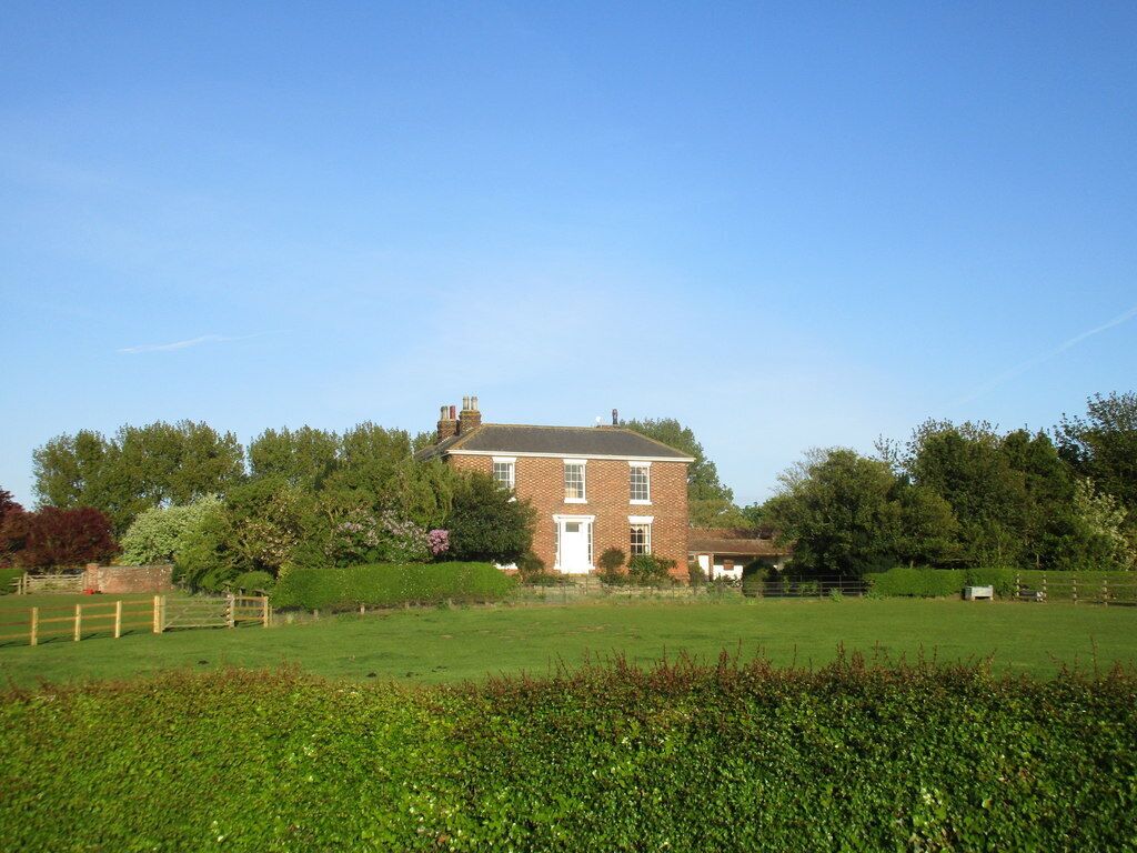 A brick house with a white door and windows, surrounded by a green field and trees.