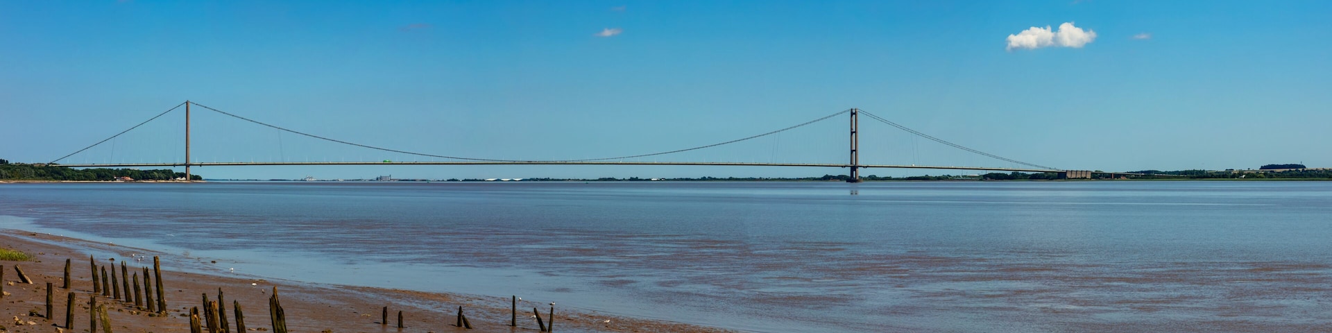 Un puente colgante sobre aguas tranquilas, con una playa arenosa al frente.