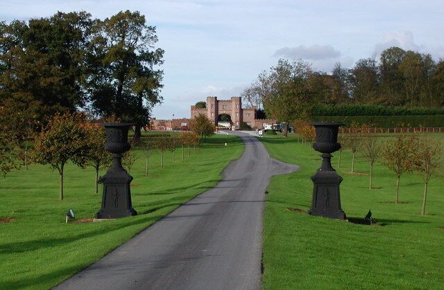 A rural road leading to a historic archway, flanked by well-maintained grass and trees.