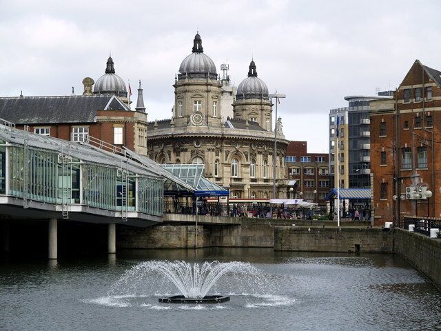 A historic building with domes, a bridge, and a fountain in a city setting.