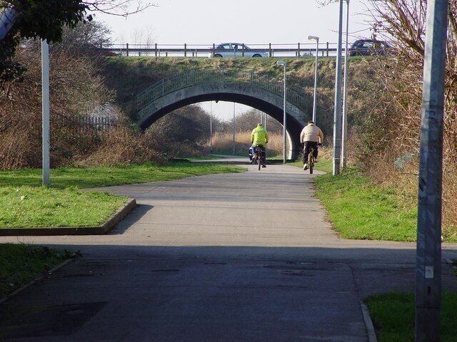 A paved path under a stone bridge with cyclists.