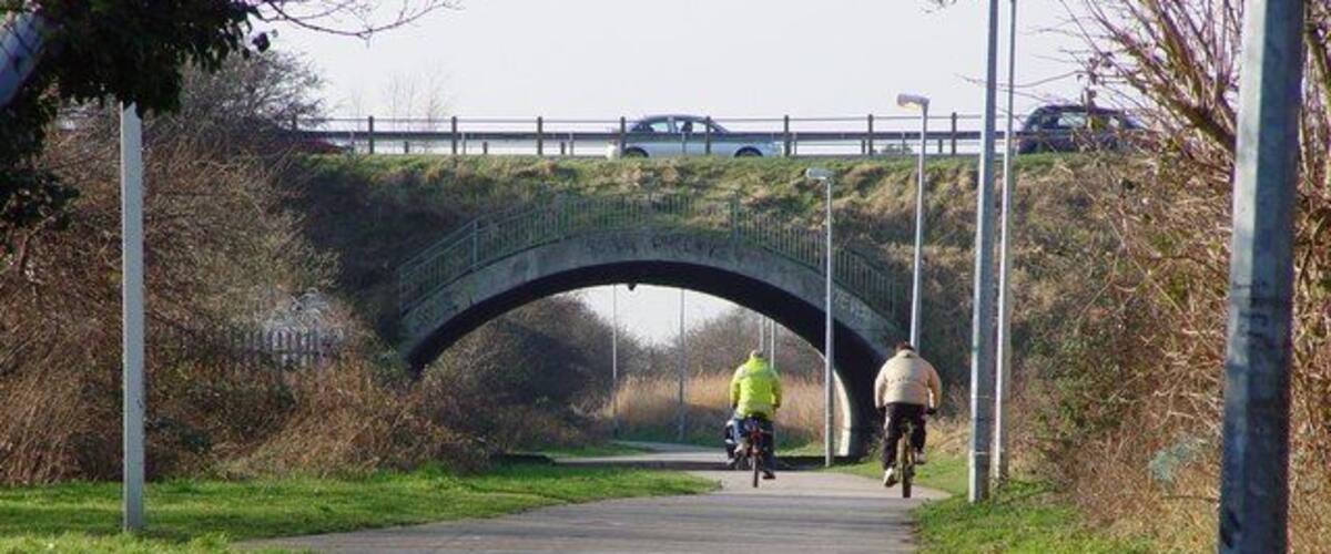 A paved path under a stone bridge with cyclists.