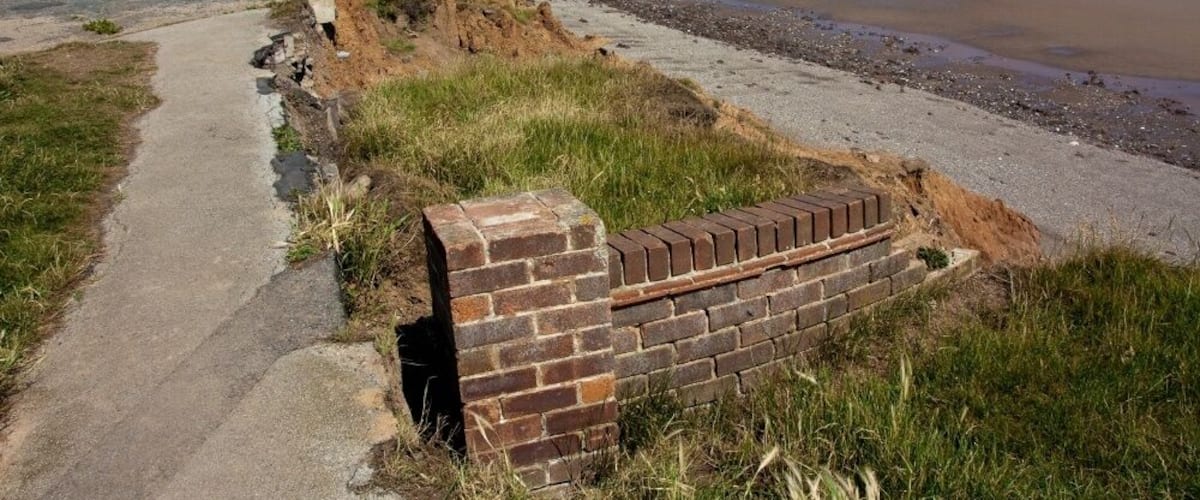 A coastal path with a brick wall and a beach in the background.