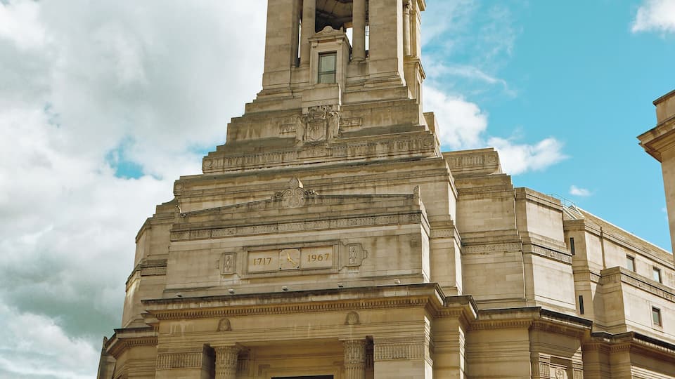 A historic building with a prominent tower and columns, surrounded by pedestrians and vehicles.
