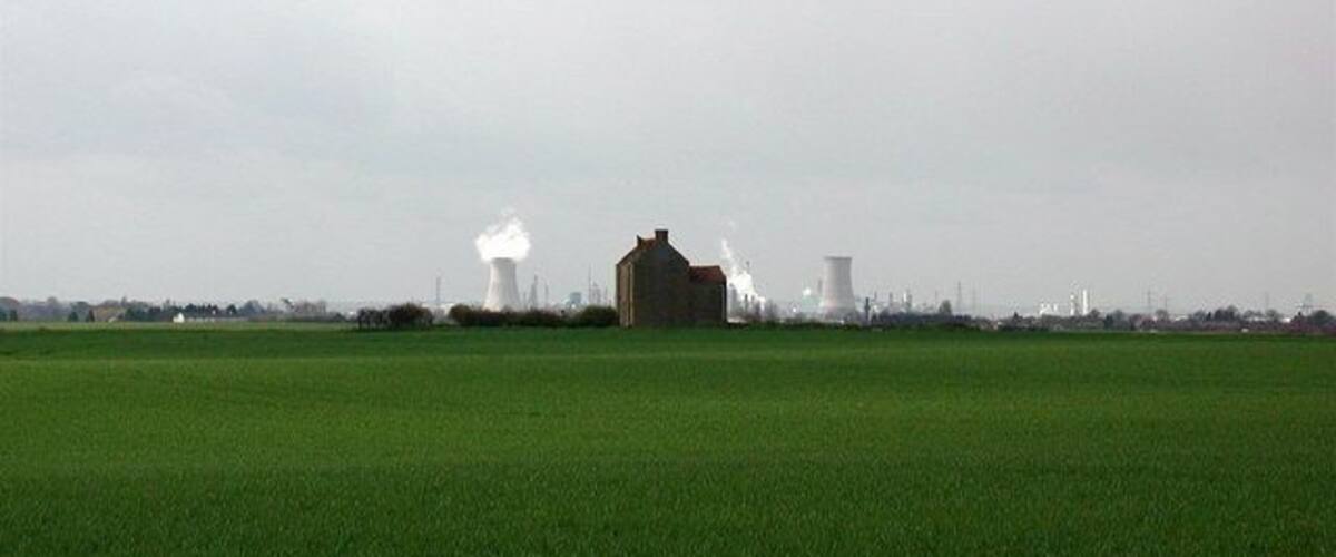A green field with a large building and industrial structures in the background.