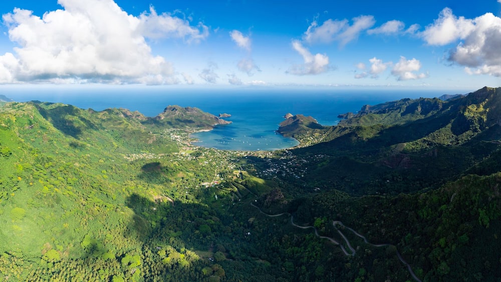 A lush green valley with a coastal town and a clear blue sky.