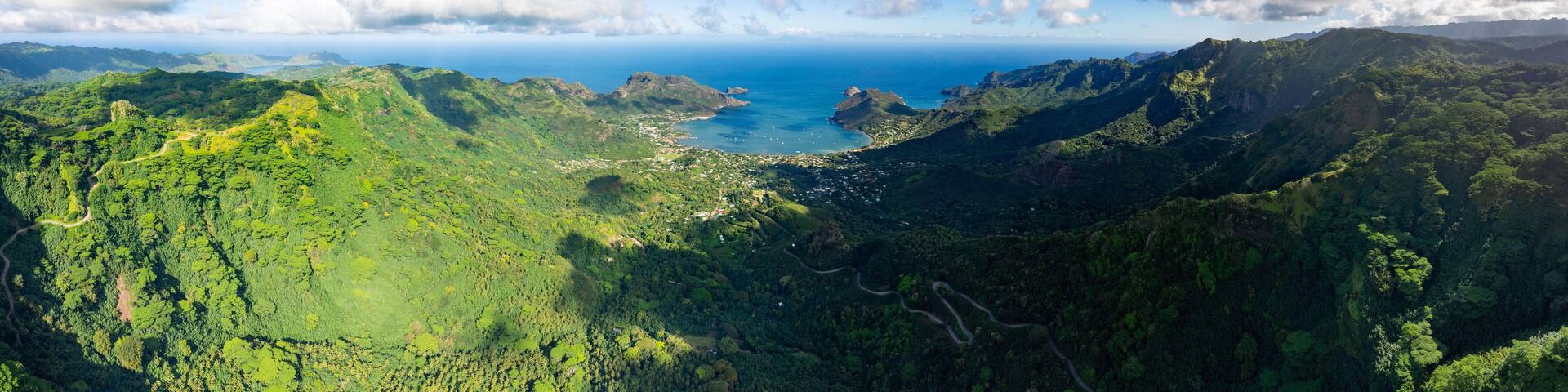 A lush green valley with a coastal town and a clear blue sky.