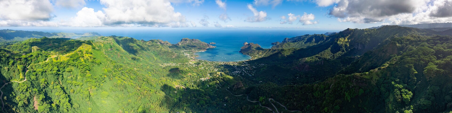 A lush green valley with a coastal town and a clear blue sky.