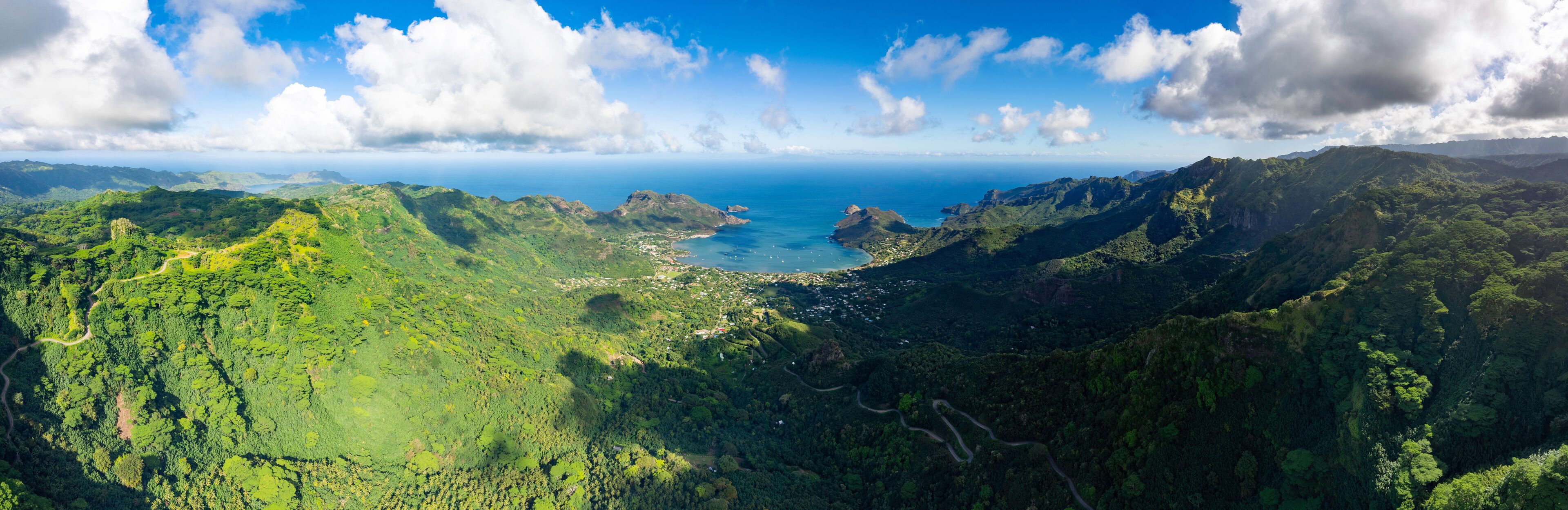 A lush green valley with a coastal town and a clear blue sky.
