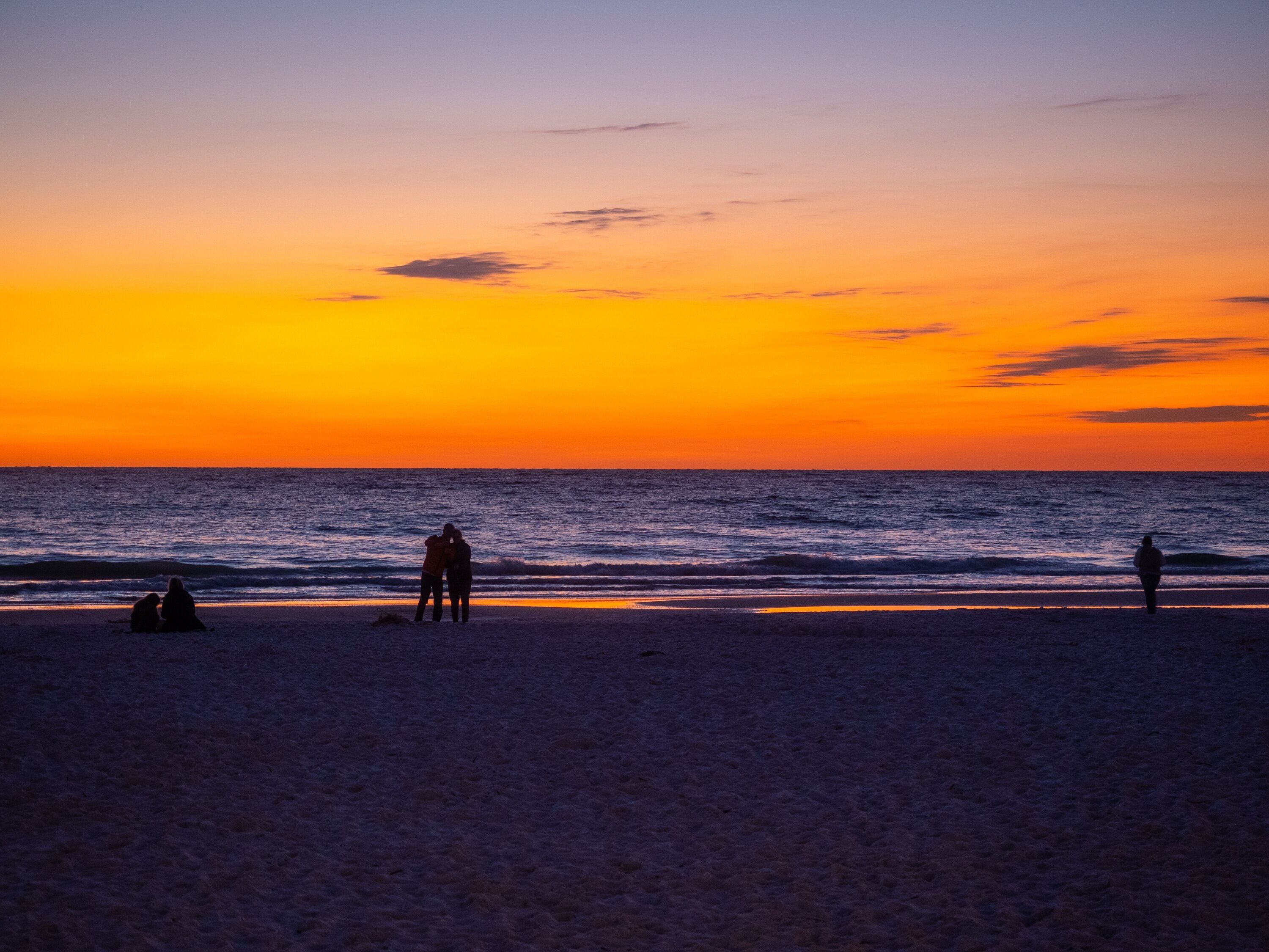 A beach at sunset with silhouettes of people and waves.