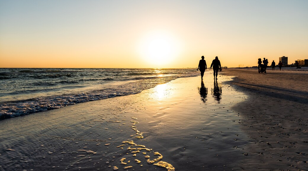 Sarasota, USA Sunset sun in Siesta Key, Florida with coastline ocean gulf of mexico on beach shore and many people couple silhouette walking by waves