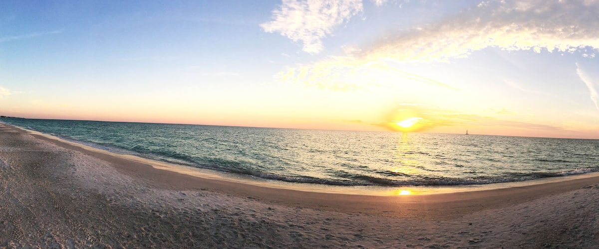 A beach with a curved shoreline, waves, and a sunset.