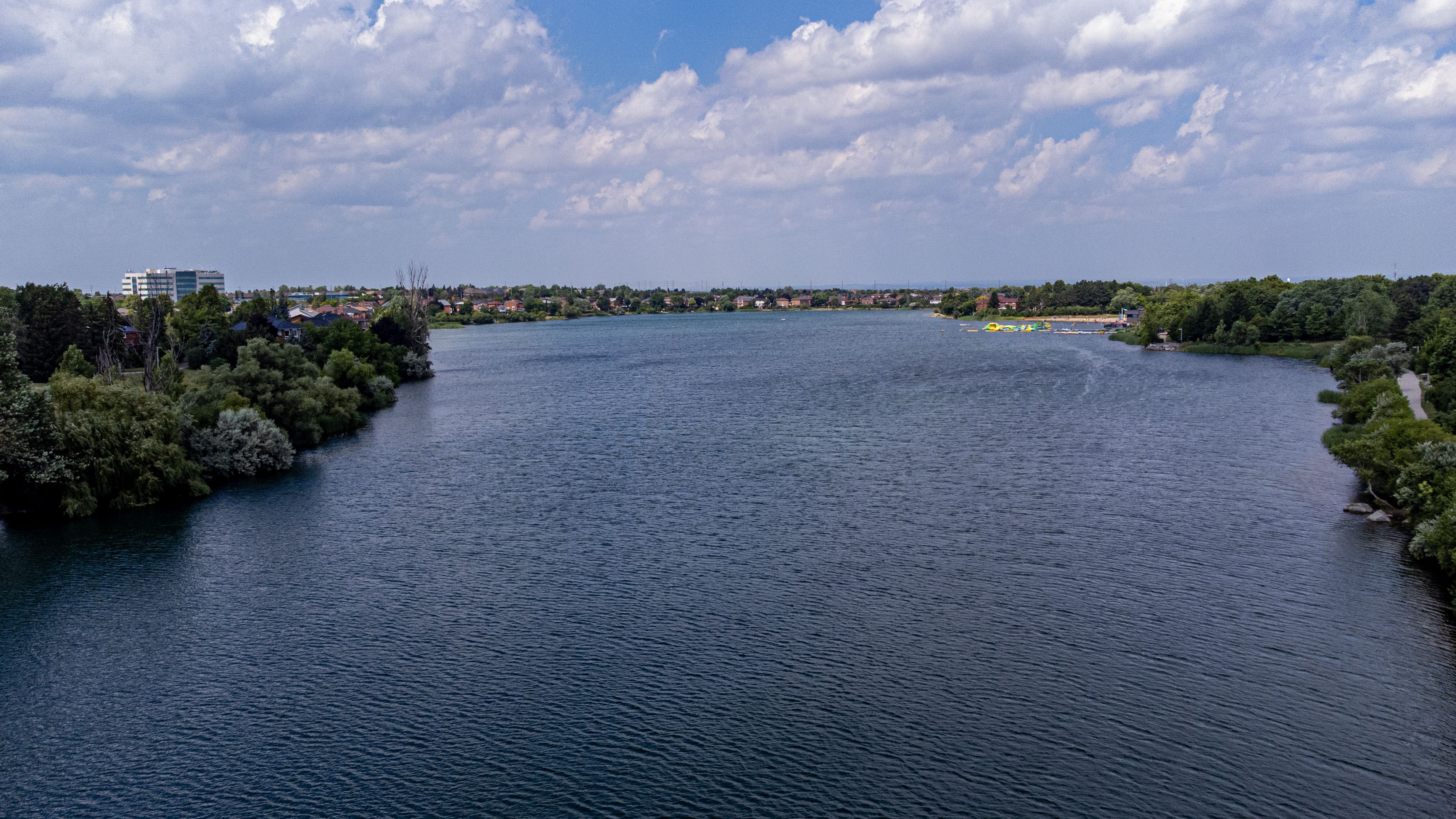 Ein Fluss, der von dichtem Grün gesäumt wird und in der Ferne eine Stadtlandschaft zeigt.