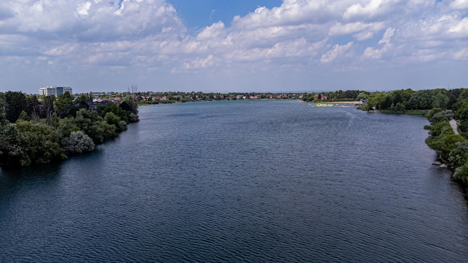 Ein Fluss, der von dichtem Grün gesäumt wird und in der Ferne eine Stadtlandschaft zeigt.