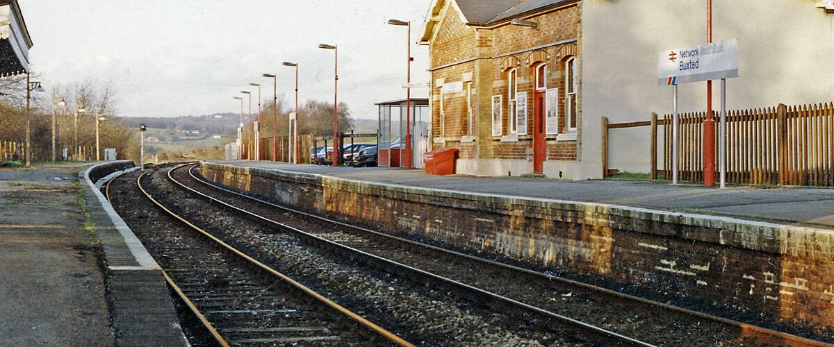 A railway station with tracks, a platform, and a building with a sign.