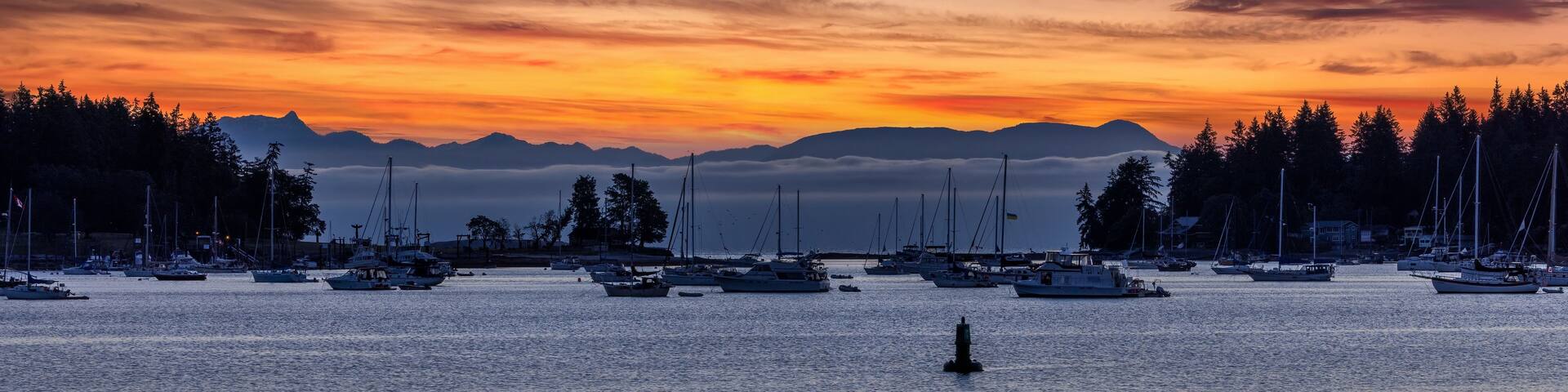 A marina with boats at sunset, mountains in the background, and a forested shoreline.