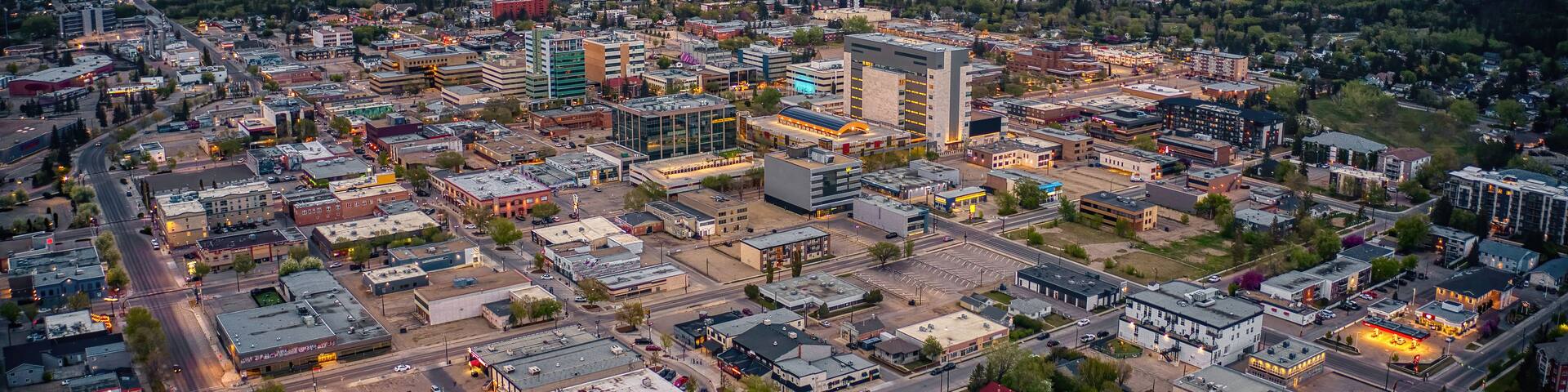 An aerial view of a city with a mix of commercial and residential buildings, a prominent shopping center, and a river in the background.