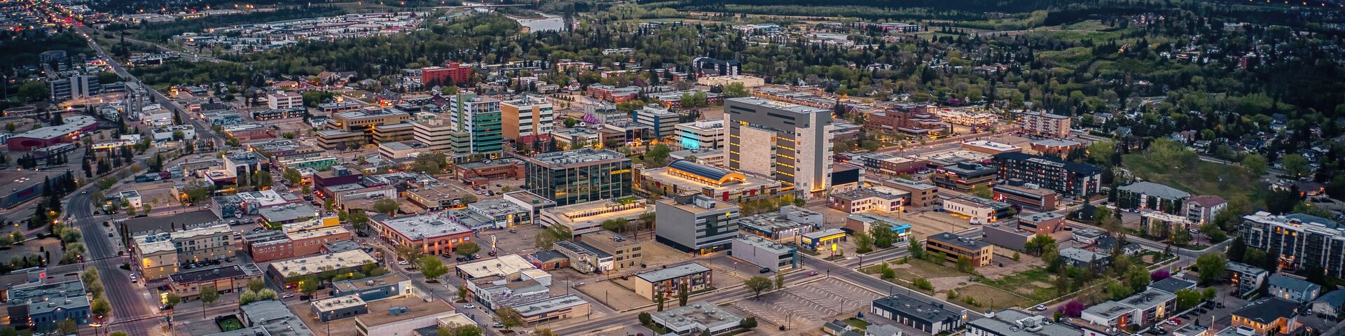 An aerial view of a city with a mix of commercial and residential buildings, a prominent shopping center, and a river in the background.