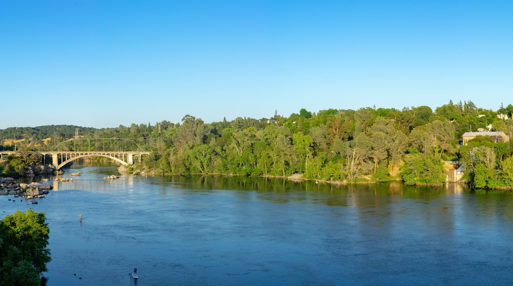 Um rio com uma ponte, vegetação exuberante e edifícios numa encosta.