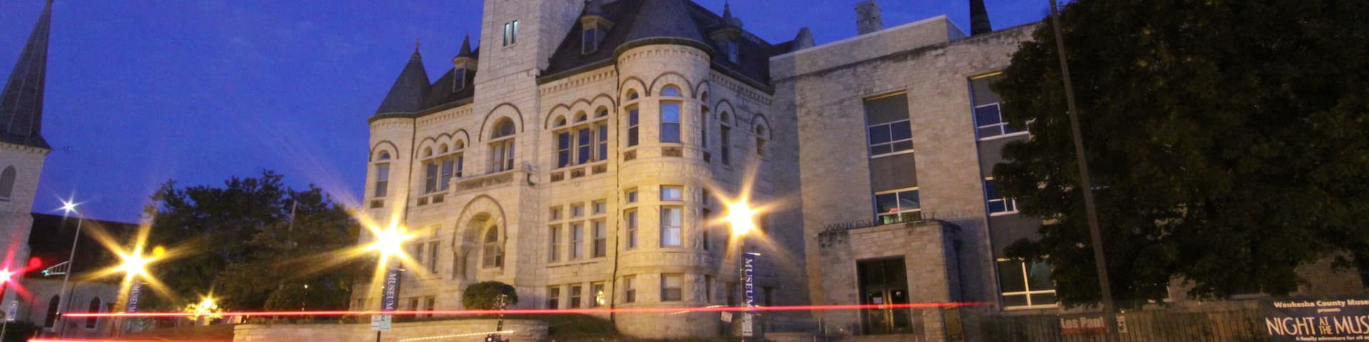 A historic building with a clock tower, illuminated windows, and a sign for the 'Night at the Museum' event.