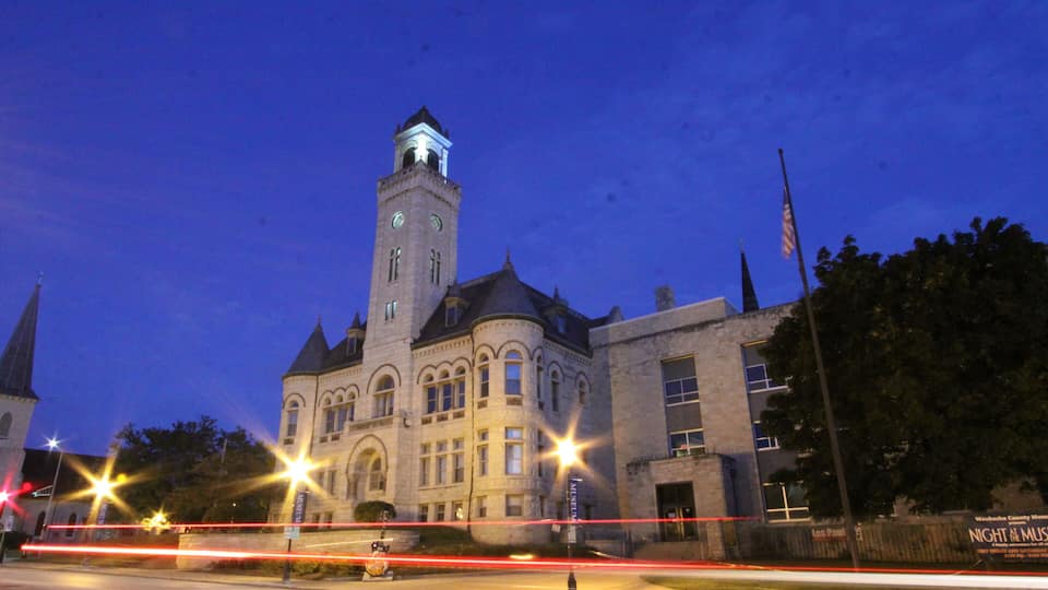 A historic building with a clock tower, illuminated windows, and a sign for the 'Night at the Museum' event.