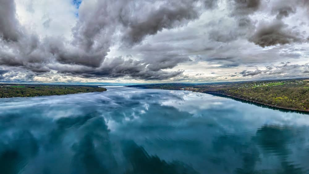 Color panorama aerial, drone, photo over Cayuga Lake, Lansing, NY, near Ithaca, on an overcast morning. Clouds reflecting on calm water surface. April 2025