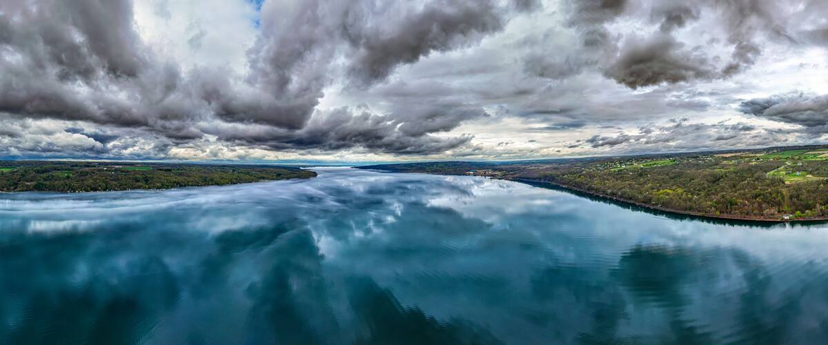 Color panorama aerial, drone, photo over Cayuga Lake, Lansing, NY, near Ithaca, on an overcast morning. Clouds reflecting on calm water surface. April 2025