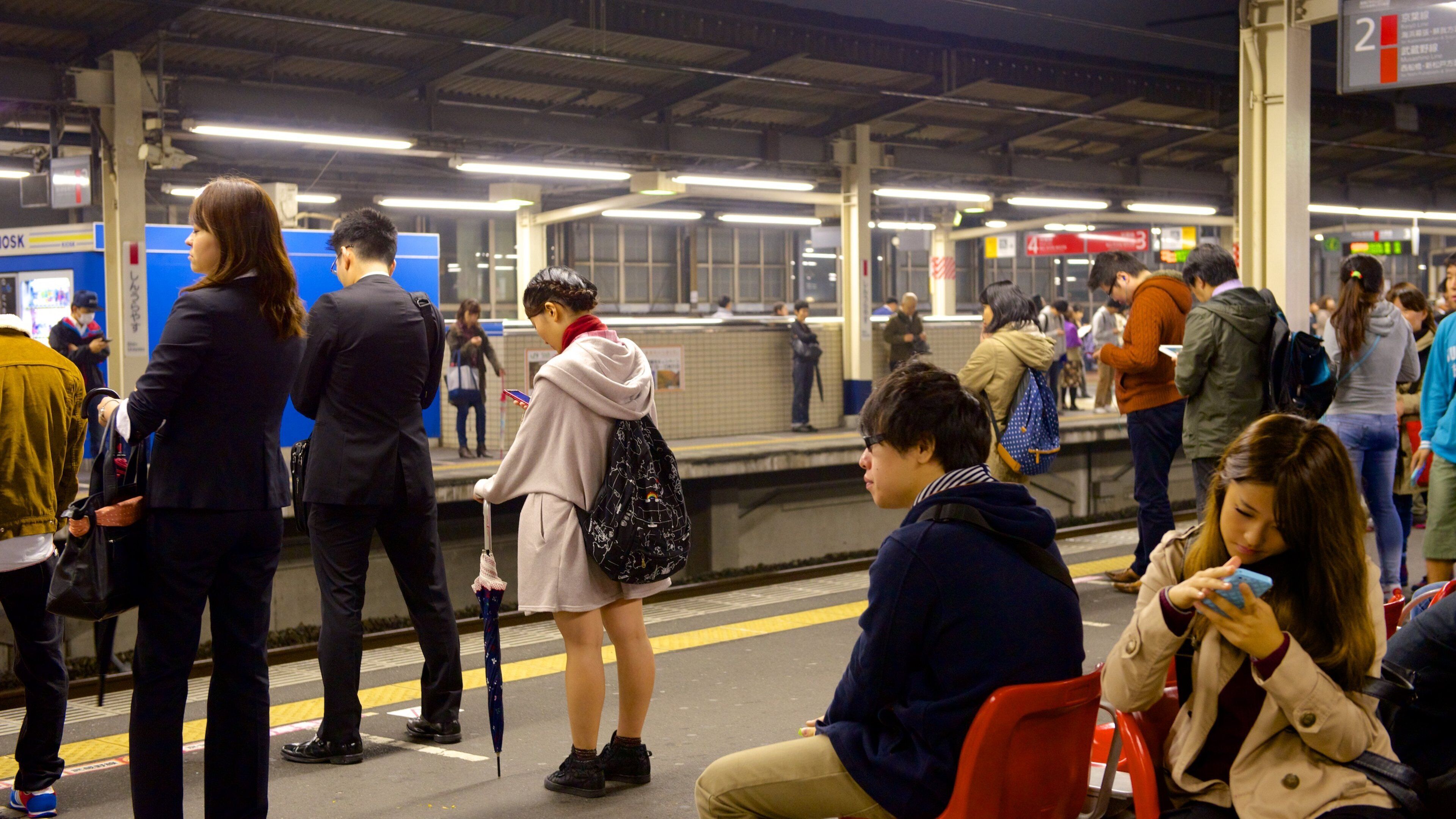 A busy subway station with people waiting and using their phones.