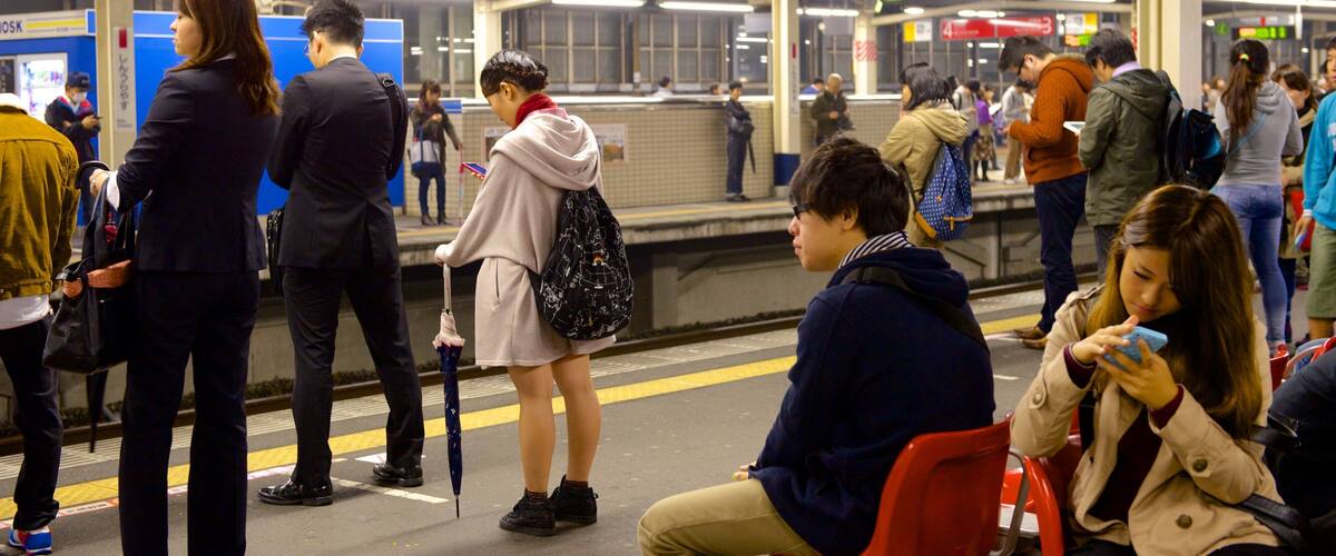 A busy subway station with people waiting and using their phones.