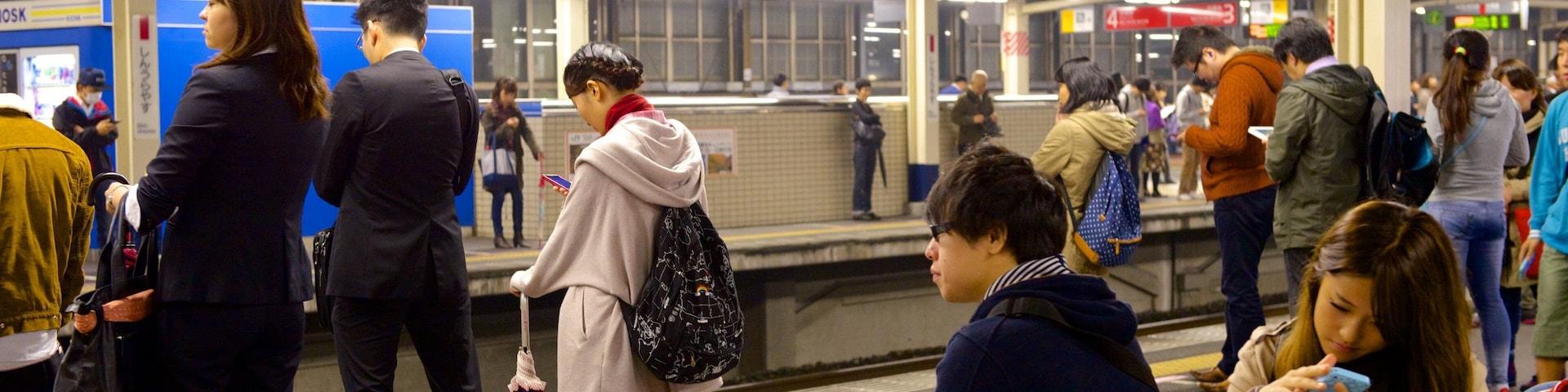 A busy subway station with people waiting and using their phones.