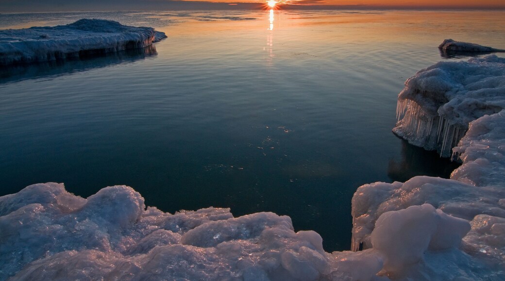 The sun rises over ice formations on the Lake Michigan shoreline on a peaceful winter morning.