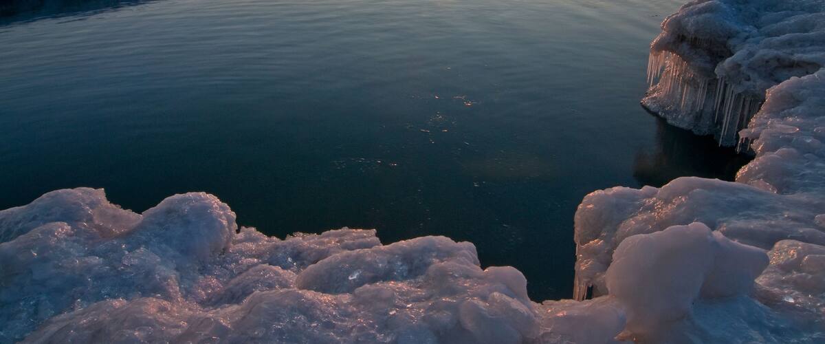 The sun rises over ice formations on the Lake Michigan shoreline on a peaceful winter morning.